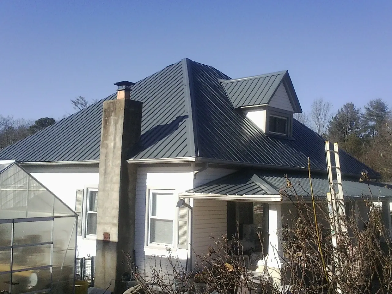 Dark blue standing seam metal roof on a white farmhouse with dormer — Slate & Tile Roof Repair by Roofing Brothers in Mandeville