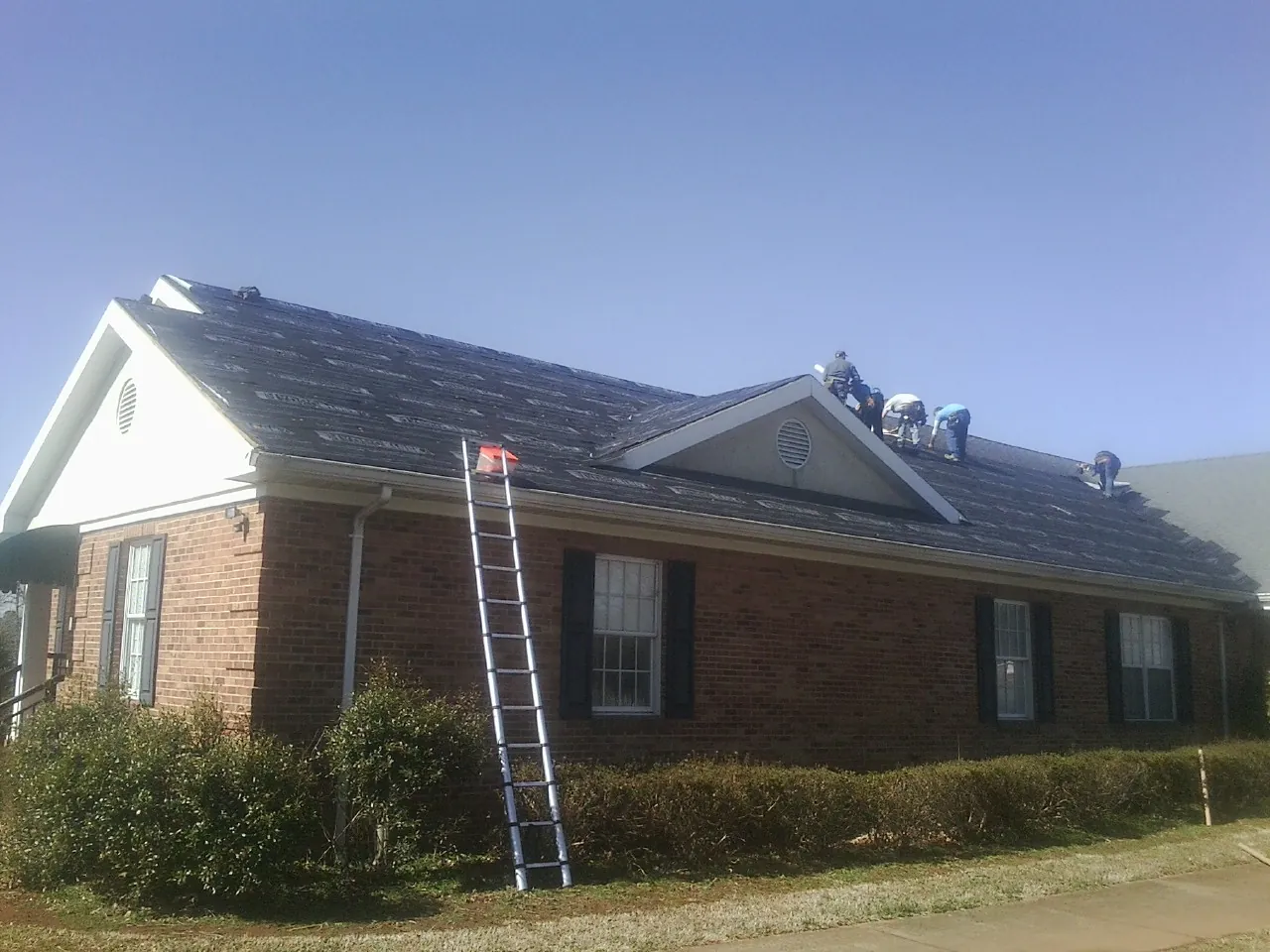 Crew tearing shingles off a brick ranch roof with a ladder set — Metal Roof Repair work by our crew in Mandeville
