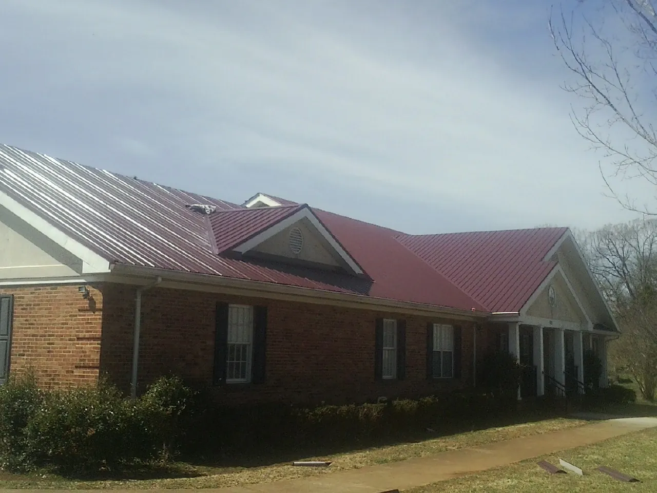 Red metal roof with gabled entries on a long brick building, from a Hail Damage Roof Repair job in Mandeville