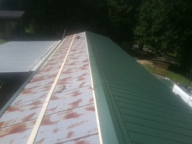 Old rusted panels beside newly installed green metal roofing — Wind Damage Roof Repair by Roofing Brothers in Mandeville