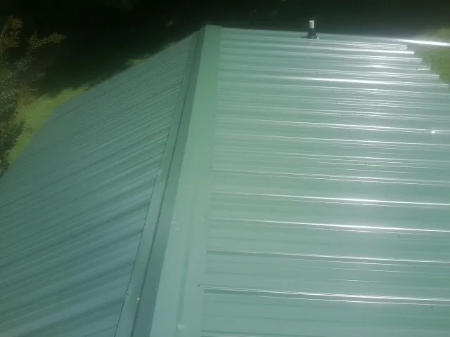 New green metal panels meeting at the ridge of a roof — Flat Roof Repair work by our crew in Mandeville