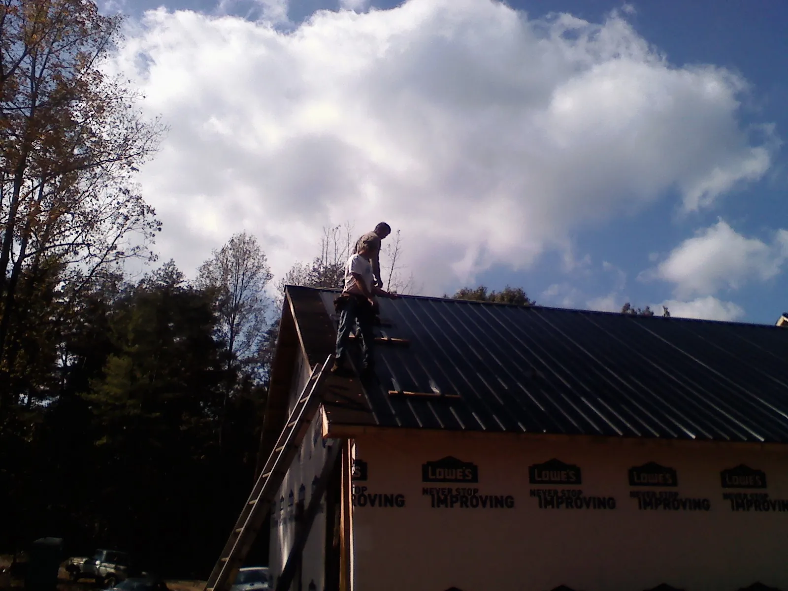 Roofer fastening dark metal panels high against a cloudy sky, from a Roof Inspection job in Mandeville