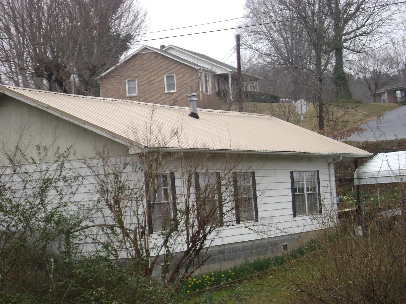 Tan metal roof on a white sided house set into a hillside — Commercial Roofing by Roofing Brothers in Mandeville